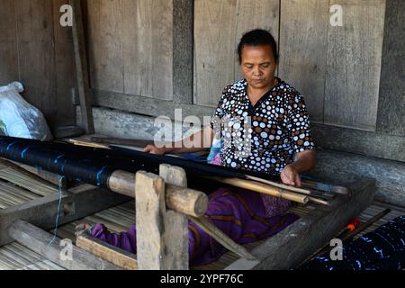 Luba, Flores, Indonesia - ottobre 31 2024: Donna che tesseva tessuti Ikat sulla sua veranda in un villaggio tradizionale. Foto Stock