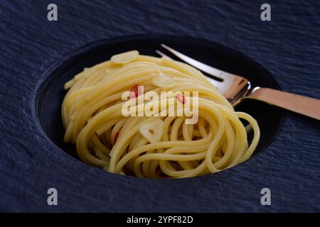Spaghetti Colatura di Alici con aglio e peperoncini su un piatto nero da vicino Foto Stock