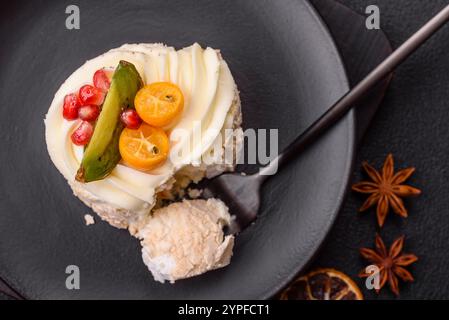 Pezzo di meringa dolce con semi di agrumi, kiwi e melograno su sfondo di cemento scuro Foto Stock