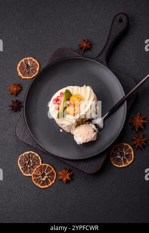 Pezzo di meringa dolce con semi di agrumi, kiwi e melograno su sfondo di cemento scuro Foto Stock