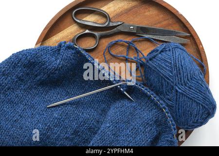 Fotografia piatta di un filato di lana blu lavorato a maglia sugli aghi di metallo con palla di filato e forbici vintage, lavorazione a maglia stockinette in prog Foto Stock