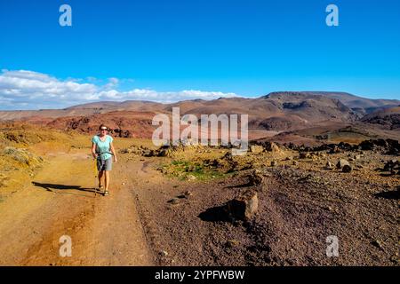 Escursionista femminile che cammina nell'arido paesaggio delle montagne anti atlante nella regione di Jebel Sirwa / Siroua in Marocco vicino al villaggio di Assaisse Foto Stock