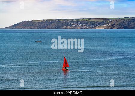 Una piccola barca a vela con vele rosse che naviga su Mounts Bay in una giornata di sole contro un mare blu Penzance Cornovaglia Inghilterra Regno Unito Foto Stock