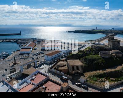 Vista aerea di Tarifa, Spagna, con una fortezza su una collina rocciosa, architettura moderna e storica e un oceano scintillante sullo sfondo. Foto Stock