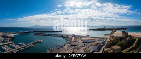 Veduta aerea di Tarifa, Spagna, con un vivace porto, spiaggie sabbiose e una struttura simile a un castello storico sotto un cielo azzurro. Foto Stock