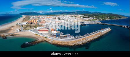 Prospettiva aerea di Tarifa, in Spagna, con un vivace porto, spiagge sabbiose, edifici imbiancati, un castello storico e le vicine turbine eoliche. Foto Stock