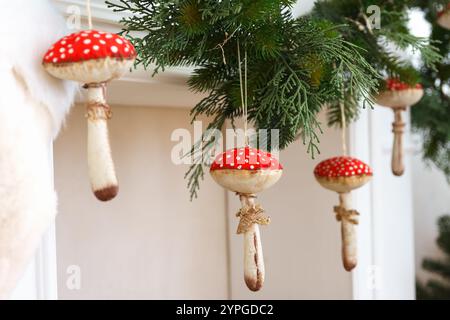 Ornamenti rustici di funghi con tappi rossi e puntini bianchi si estendono da una ghirlanda verde, creando una calda atmosfera di vacanza. Lo sfondo morbido si aggiunge a. Foto Stock