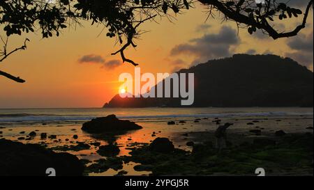 Tramonto su una spiaggia tranquilla con ombre scure e sgranate sulle rocce. Foto Stock