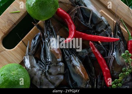 Una bella mostra di gamberi tigre si appoggia su foglie di banana, accompagnati da zeli verdi e peperoncini rossi. Foto Stock