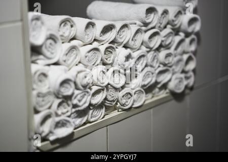 Asciugamani bianchi arrotolati disposti in modo ordinato su uno scaffale in un bagno rilassante Foto Stock