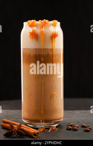 Preparazione del latte di zucca speziato in una tazza trasparente, versare il latte montato, foto ampia. Su sfondo nero. Nelle vicinanze c'è un bastone di cannella e scat Foto Stock