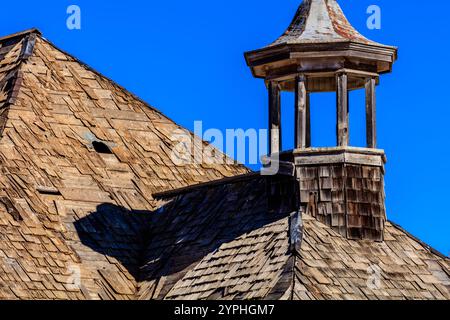 Un tetto con un camino in cima. Il tetto è fatto di tegole di legno. Il camino è vecchio e ha un aspetto rustico. Il cielo è blu e limpido Foto Stock