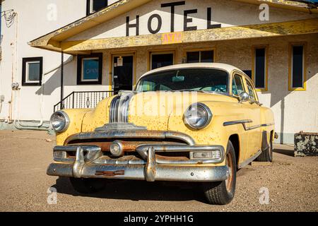 Un'auto gialla è parcheggiata di fronte a un hotel. La macchina è vecchia e arrugginita. L'hotel è giallo e ha un cartello con scritto "Hotel". La scena è ambientata Foto Stock