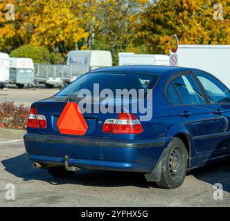 Un trattore di colore blu è parcheggiato molto, con una caratteristica forma triangolare arancione sul retro. Gli alberi circostanti mostrano vivaci colori autunnali sotto Foto Stock
