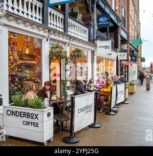 Persone sedute all'aperto a mangiare e bere nei caffè sul marciapiede della città di Chester nel Cheshire a natale su Bridge Street Foto Stock