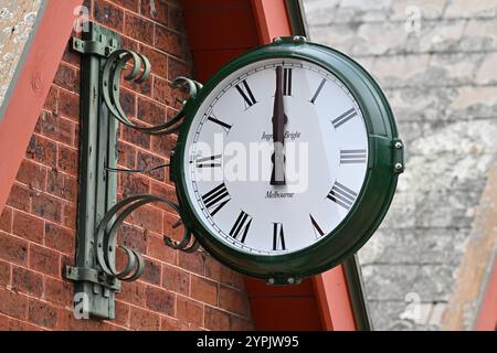 Ingrams verde luminoso orologio analogico, con quadrante bianco e numeri romani neri, con lancette a ore 12, attaccato a una parete di mattoni rossi Foto Stock