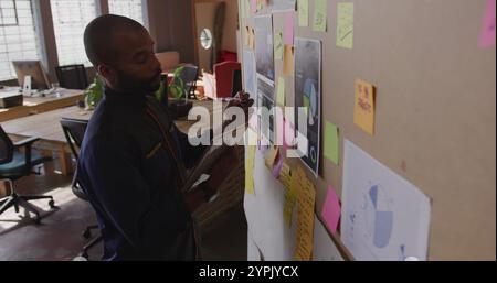 Vista laterale ad angolo alto di un giovane professionista birazziale creativo in un ufficio moderno utilizzando tablet com Foto Stock