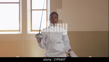 Ritratto di un'atleta birazziale di schermitrice durante un allenamento di scherma in una palestra, camminando wea Foto Stock