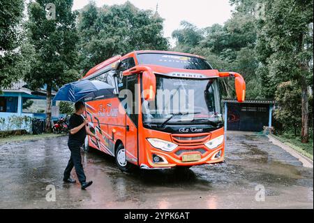 Bogor, 18 novembre 2024. Un autobus rosso entra nell'area parcheggio di una villa, circondato da vegetazione lussureggiante e dintorni panoramici Foto Stock