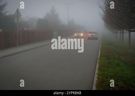 Vettura che viaggia su strade nebbiose con fari o fari accesi. Bassa visibilità - guida pericolosa delle auto in inverno in condizioni meteorologiche avverse Foto Stock