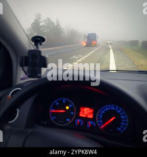 Vettura che viaggia su strade nebbiose con fari o fari accesi. Bassa visibilità - guida pericolosa delle auto in inverno in condizioni meteorologiche avverse Foto Stock