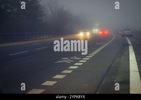 Vettura che viaggia su strade nebbiose con fari o fari accesi. Bassa visibilità - guida pericolosa delle auto in inverno in condizioni meteorologiche avverse Foto Stock