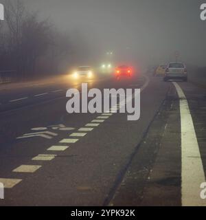 Vettura che viaggia su strade nebbiose con fari o fari accesi. Bassa visibilità - guida pericolosa delle auto in inverno in condizioni meteorologiche avverse Foto Stock