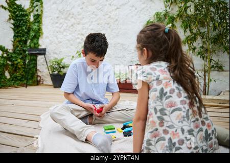 Due bambini si divertono a costruire momenti divertenti con blocchi colorati su un ponte di legno. Circondati da una vegetazione lussureggiante, condividono un momento gioioso e creativo Foto Stock