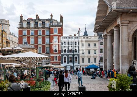 Il mercato di Covent Garden, animato da visitatori sotto la storica architettura georgiana, caffetterie all'aperto e artisti di strada, creano un'atmosfera vivace Foto Stock