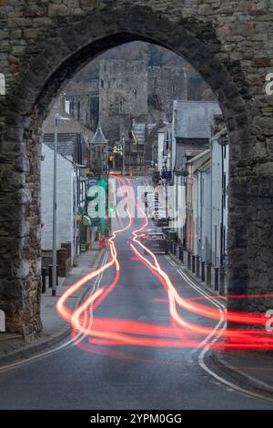 L'auto si illumina attraverso un arco nelle mura della città che mostra il castello di Conwy, Galles Foto Stock