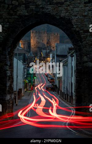 L'auto si illumina attraverso un arco nelle mura della città che mostra il castello di Conwy, Galles Foto Stock