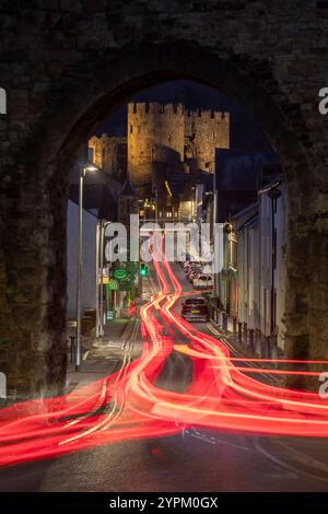 L'auto si illumina attraverso un arco nelle mura della città che mostra il castello di Conwy, Galles Foto Stock