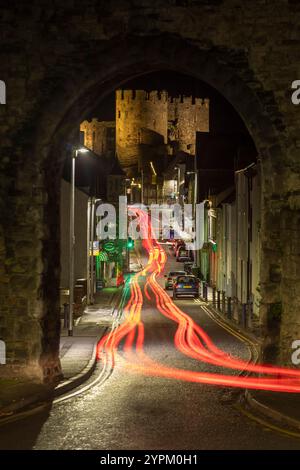 L'auto si illumina attraverso un arco nelle mura della città che mostra il castello di Conwy, Galles Foto Stock