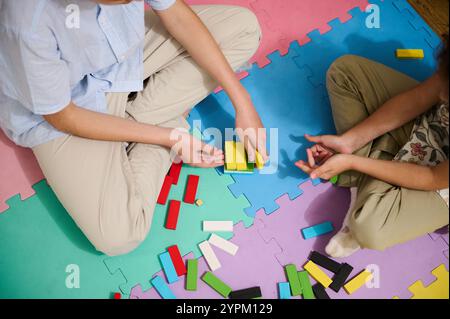 Due bambini si impegnano in un'attività ludica di costruzione utilizzando blocchi colorati su un tappetino in schiuma. Questa immagine cattura l'essenza di creato Foto Stock