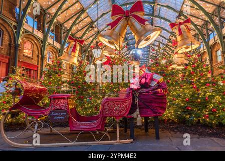 La scena natalizia di Covent Garden presenta una slitta festosa, torreggianti alberi di Natale, campane dorate, luci scintillanti delle fate e vivaci decorazioni a lo Foto Stock