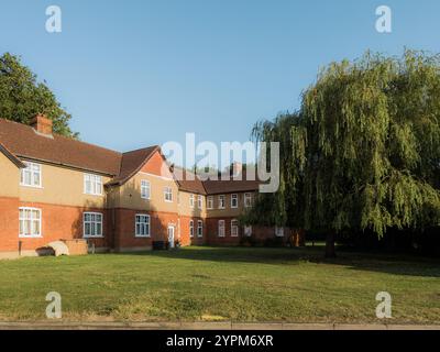 Tradizionale alloggio suburbano con una facciata in mattoni rossi, lussureggiante prato verde e un grande salice sotto un cielo azzurro Foto Stock