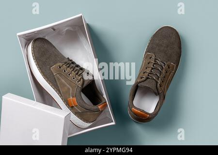 Scarpe in tela cachi in scatola su sfondo blu argento. Un paio di nuove sneaker in tessuto marrone con suola bianca per un'aderenza perfetta. Scarpe sportive comode. Foto Stock