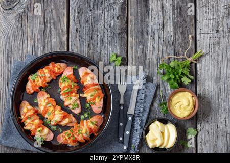 Uunimakkara, al forno con salsicce ricoperte di formaggio, pomodori e senape in piatto da forno su tavola di legno grigio con ingredienti, ricetta finlandese retrò, Foto Stock