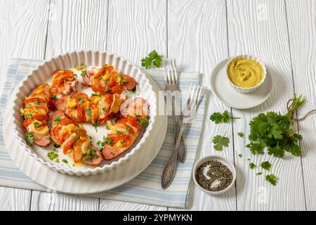 Uunimakkara, al forno con salsicce ricoperte di formaggio, pomodori, coriandolo, senape in piatto da forno su tavola di legno bianco con ingredienti, classe finlandese Foto Stock