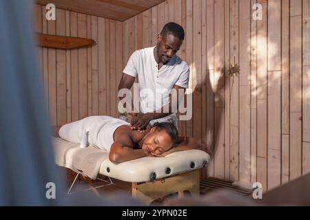 Donna afro-americana serena e sorridente a occhi chiusi che si rilassa in una spa mentre si fa un massaggio alla schiena. Foto Stock