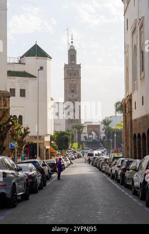 Vivace strada nel quartiere Habous di Casablanca, in Marocco, con auto parcheggiate su entrambi i lati e un'importante moschea con un alto minareto sul retro Foto Stock