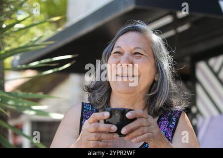 donna latina anziana che beve caffè o tè all'aperto nelle soleggiate giornate estive Foto Stock