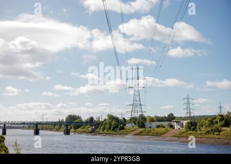 Newcastle Regno Unito: 5 luglio 2024: Newburn Riverside Park. Paesaggio del fiume Tyne con vegetazione lussureggiante e linee elettriche sotto un cielo parzialmente nuvoloso Foto Stock