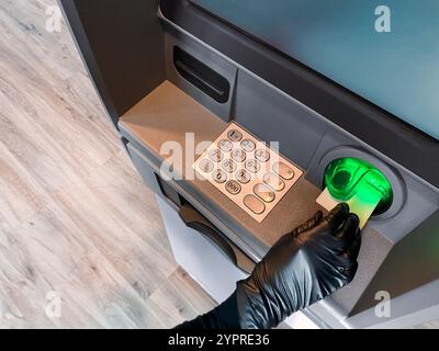 Mano ladra con guanto nero che ruba denaro. Ladro che sta commettendo rapina. Crimine finanziario. Sportello Bancomat hacking. Sistema di rottura. Prelievo di contanti allo sportello Bancomat Foto Stock