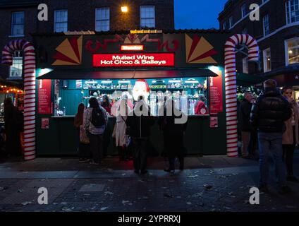La folla si riunisce in una bancarella festosa del mercato che offre VIN brulé cioccolata calda e bailey durante una serata nella stagione delle vacanze invernali York Regno Unito dicembre 2024 Foto Stock