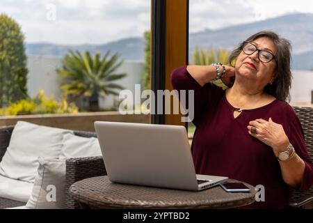 Una donna latina con il suo laptop che le sta soffrendo il collo dopo una giornata di lavoro. Concetto di stanchezza sul lavoro Foto Stock