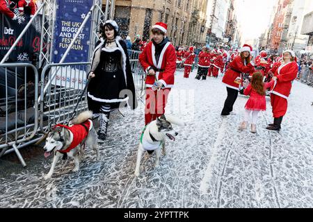 Una giovane coppia con cani partecipa al Liverpool Santa Dash 2024. I partecipanti indossati in rosso (e blu) Santa Suits corrono lungo un percorso di 5 km intorno al centro di Liverpool a sostegno del Claire House Children's Hospice. 8.500 persone hanno preso parte al 20 ° annuale Liverpool Santa Dash. Foto Stock