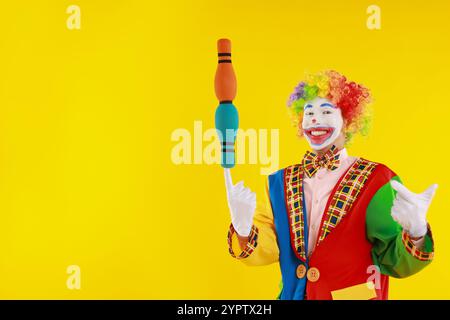 Clown felice con mazze da giocoliere su sfondo giallo, spazio per il testo Foto Stock