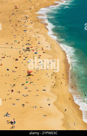 Vista aerea della spiaggia di praia de nazare che mostra i turisti che si rilassano, prendono il sole e nuotano nell'oceano durante le vacanze estive a nazare, in portogallo Foto Stock