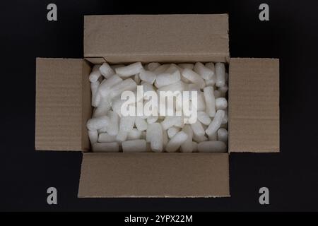 Scatola di cartone riempita con polistirene bianco su sfondo nero, progettata per proteggere gli articoli fragili durante la spedizione Foto Stock